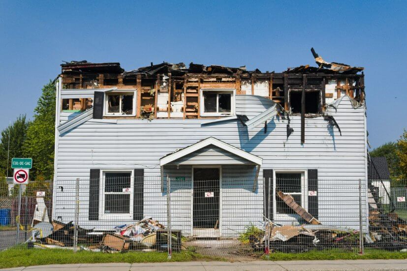 A house with a burned out upper story and debris from a house fire in the front yard.